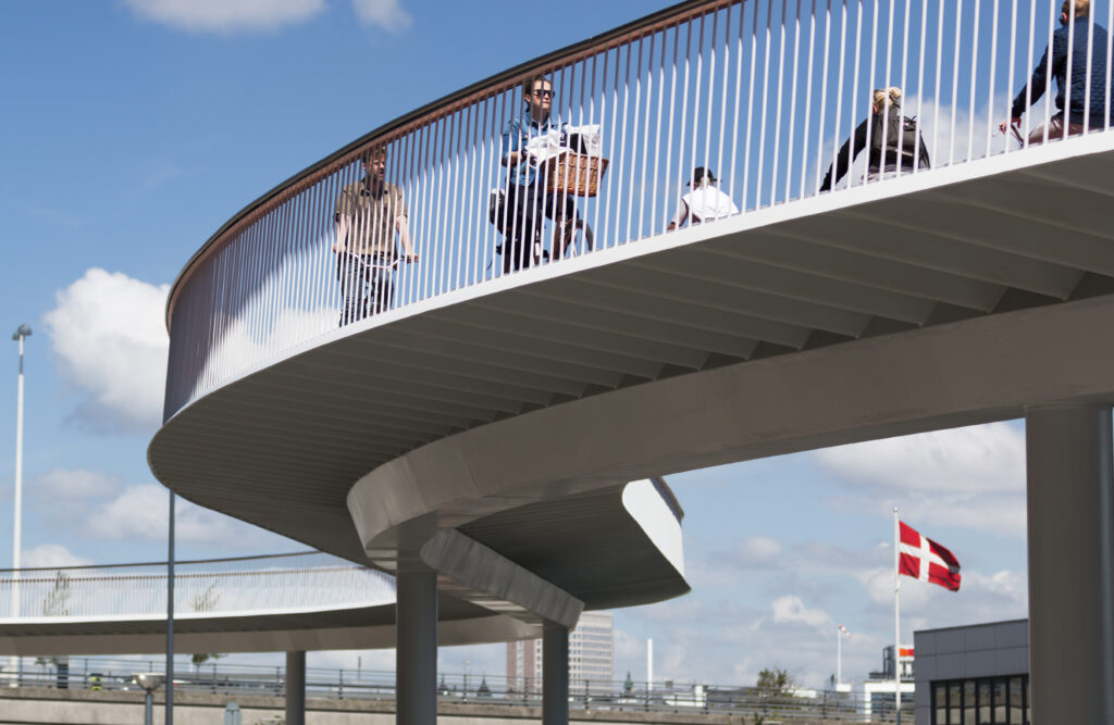 Copenhagen, Denmark - June 30, 2014: Bicycle bridge in Copenhagen, Denmark. Danish flag. Several cyclists on bicycle bridge crossing Copenhagen Harbour. Danish flag, Dannebrog, in the background.