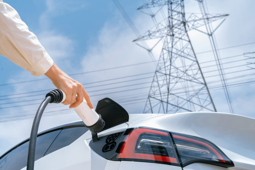 Closeup woman recharge EV electric car battery at charging station connected to electrical power grid tower on sky background as electrical industry for eco friendly vehicle utilization. Expedient